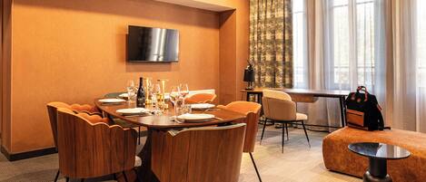 Une chambre d’hôtel comprenant un coin repas, un téléviseur fixé au mur, un canapé et une table sur laquelle se trouve un sac à dos.