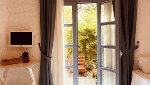 A hotel room with a bed, a desk with a TV, a chandelier, and a view of the outdoors. - Mina Otel by Adda Alaçatı (Cesme)