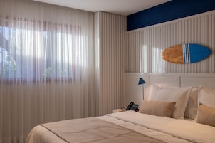 Una habitación de hotel con una cama, un teléfono en la mesita de noche y una tabla de surf en la pared.