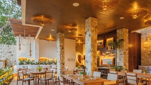Un restaurante con mesas y sillas de madera, pilares de piedra y lámparas colgantes.