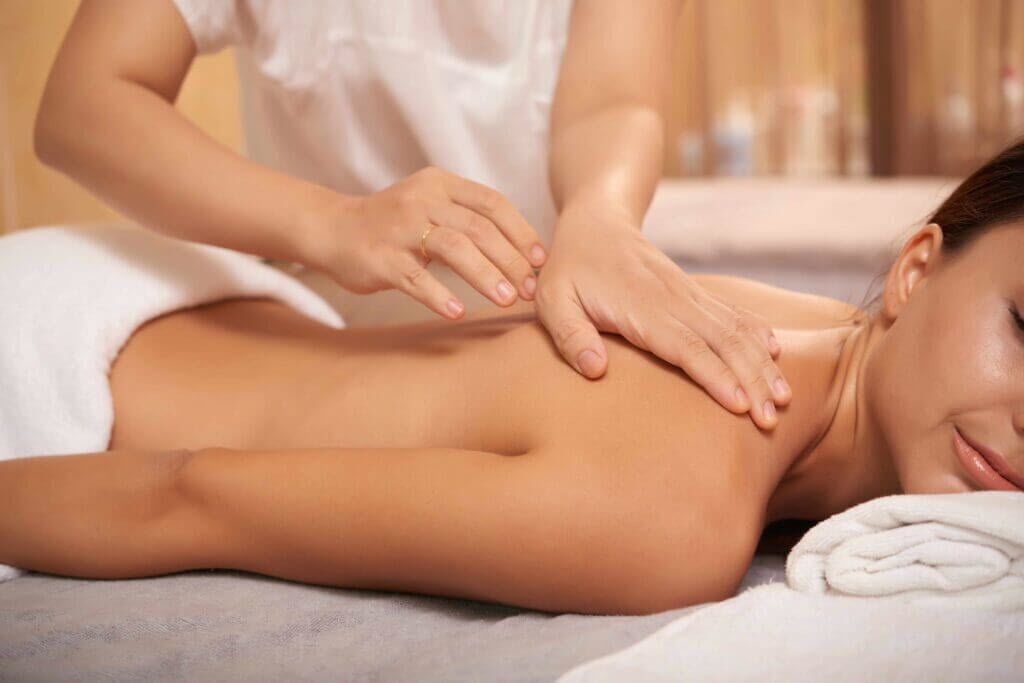 A person receiving a massage in a room with a bed and a white towel.
