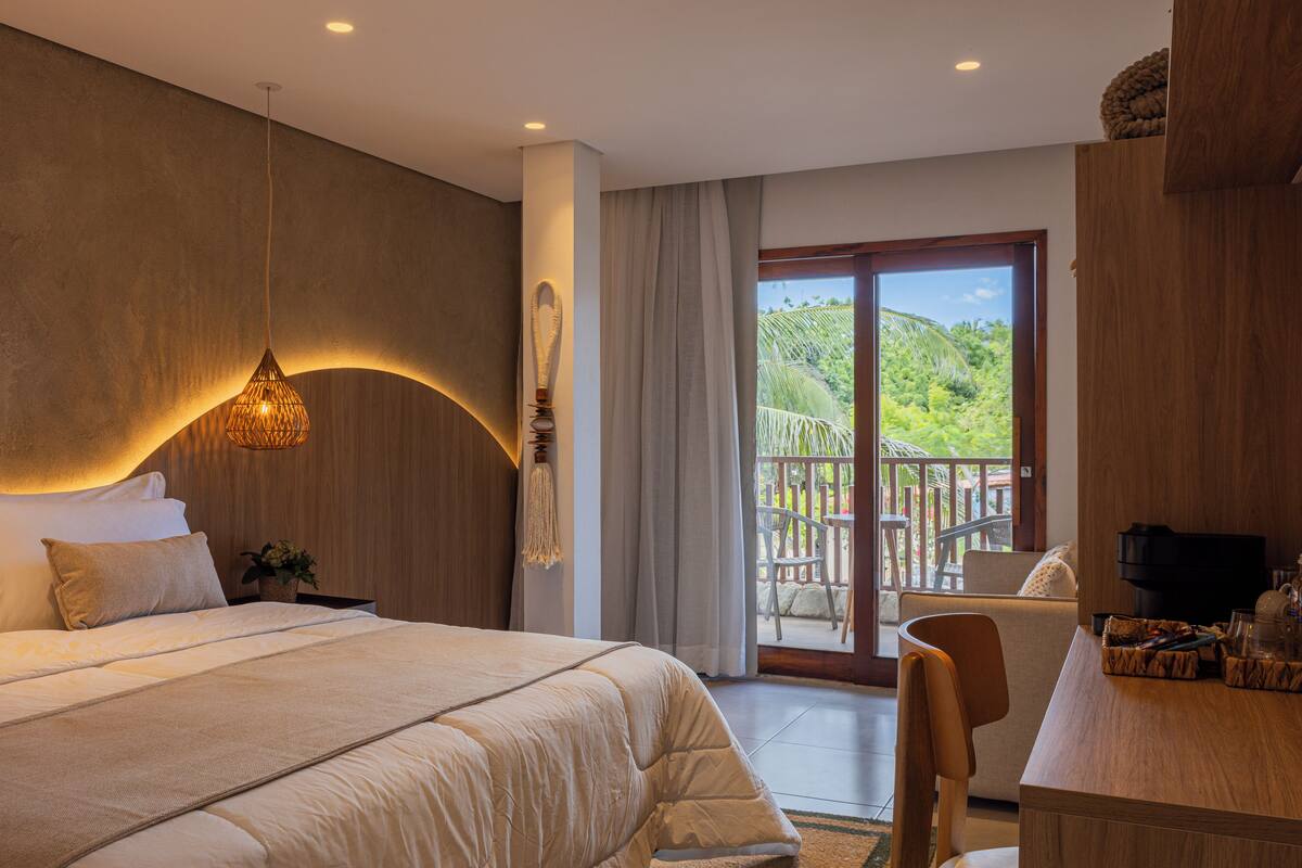 Quarto com uma cama grande, uma escrivaninha e uma varanda com vista para o verde.