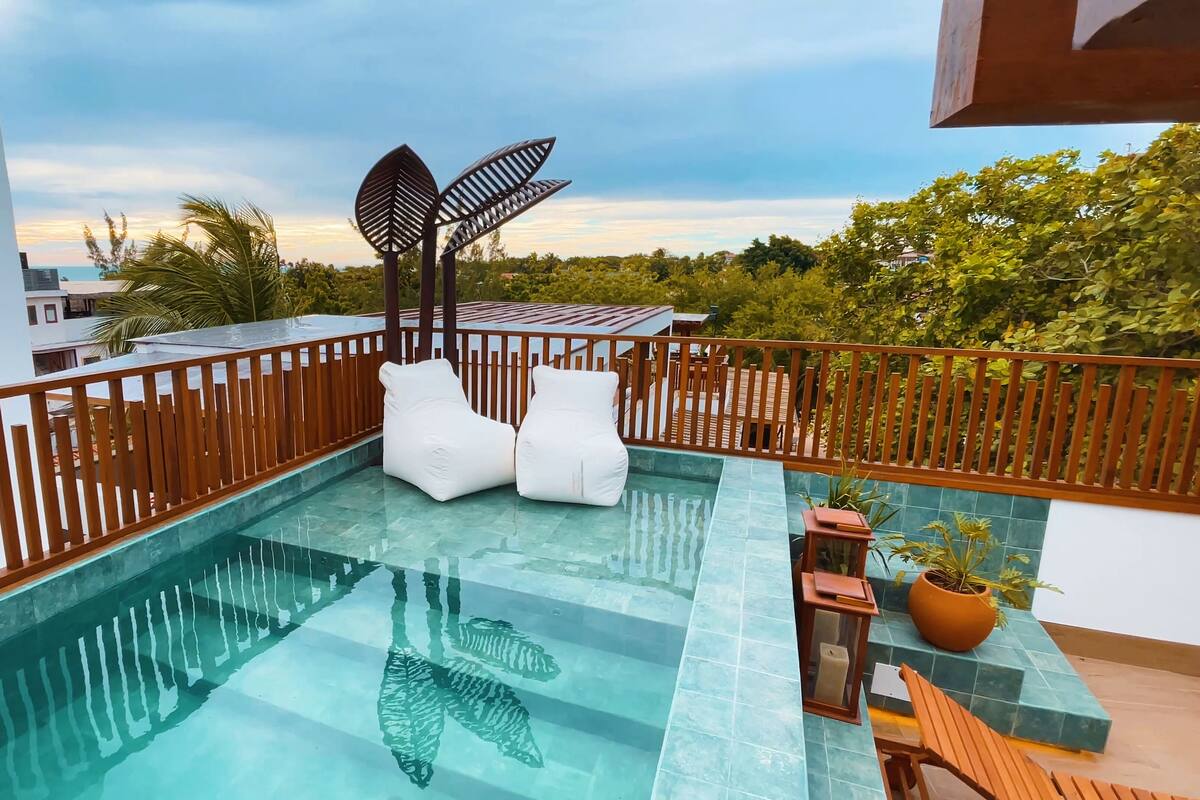 Piscina infinita no terraço, com espreguiçadeiras brancas e deck de madeira.