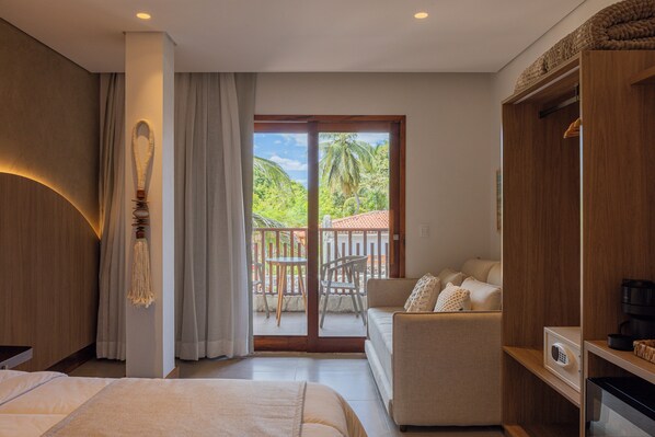 Un dormitorio con cama, sofá, armario y balcón con vistas a la vegetación.