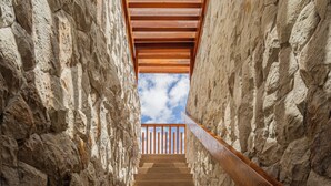 Una escalera con paredes de piedra y barandillas de madera que se eleva hacia un cielo azul.