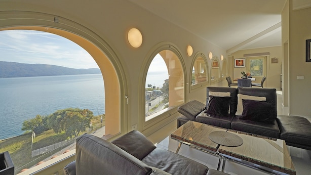 A modern living room with a large window overlooking a lake, a sofa, and a coffee table. - Your Breathtaking Penthouse (Gargnano)