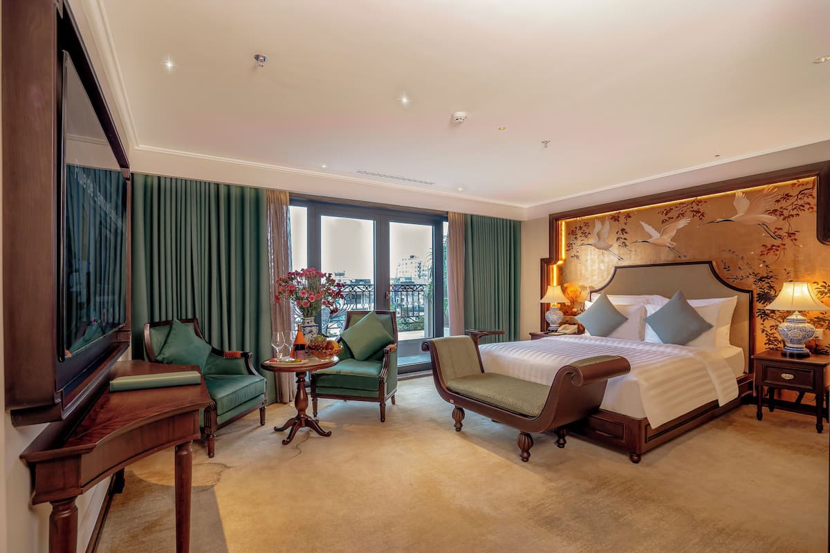 A hotel room with a large bed, two armchairs, a small table, and a TV.