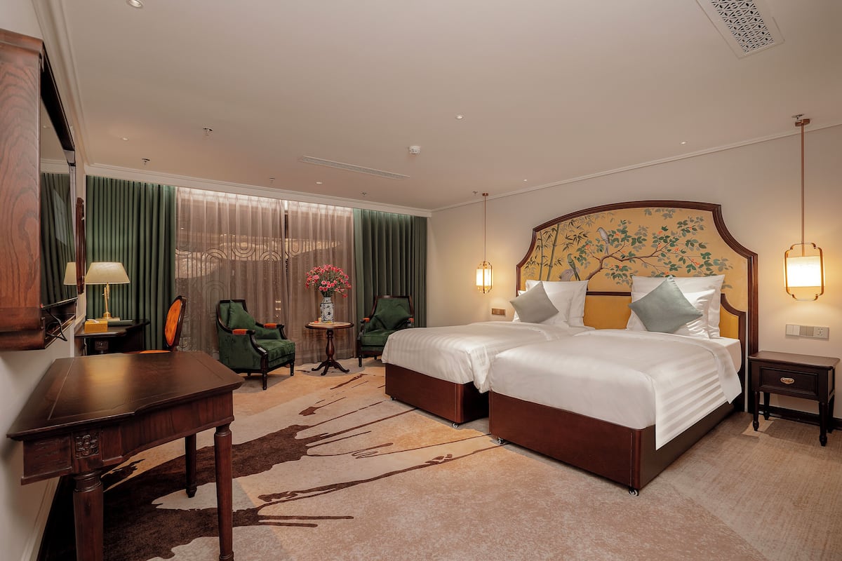 A hotel room with a large bed, two chairs, a desk, and a small table with a lamp.