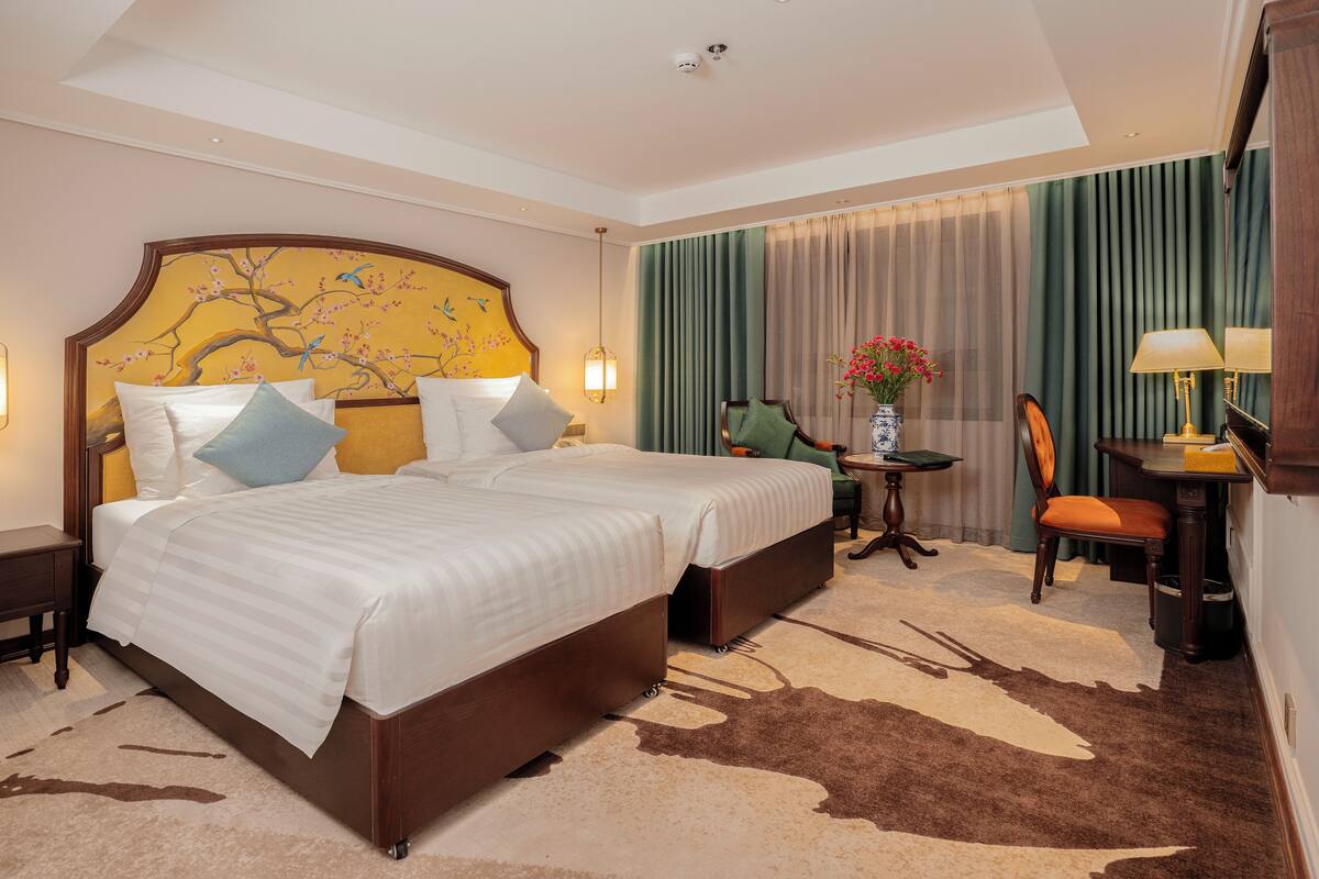 A hotel room with a large bed, two bedside tables, a chair, a desk, and a vase with flowers.