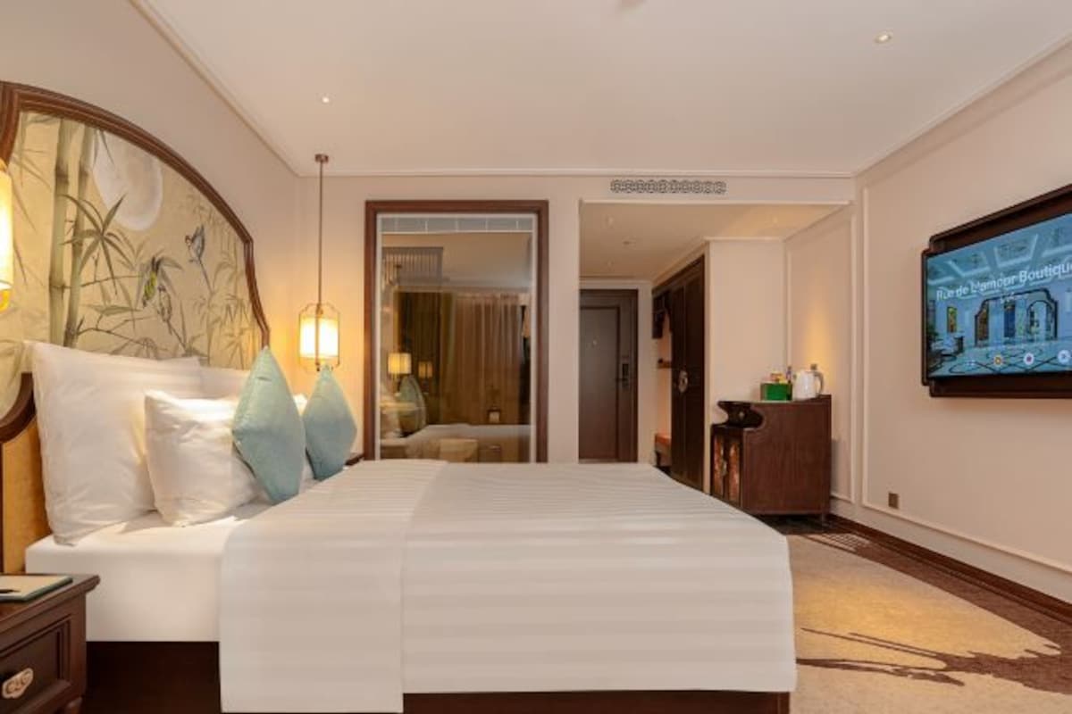 Una habitación de hotel con una cama grande, una mesita de noche, un aparador, un espejo y un televisor montado en la pared.