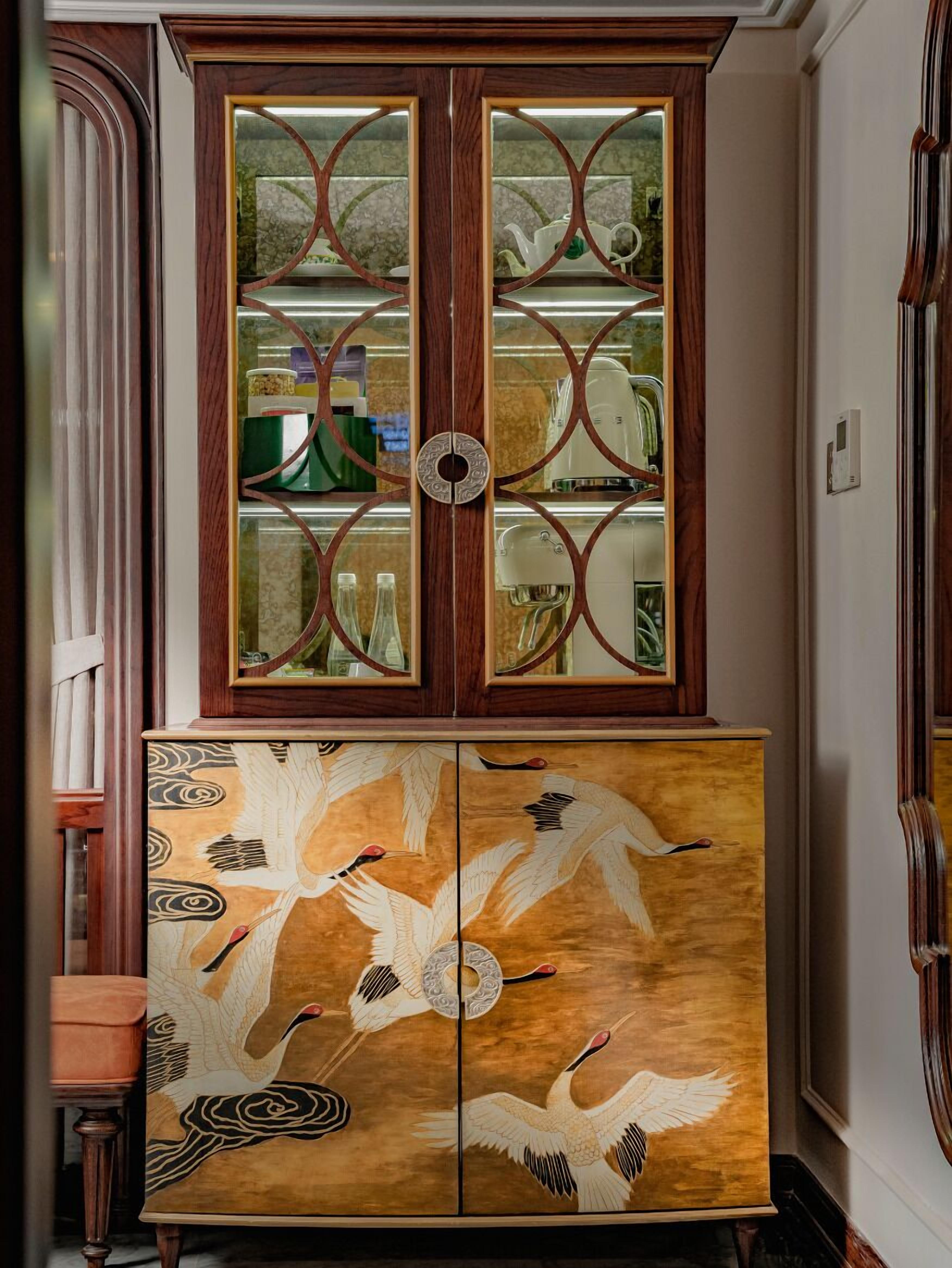 A wooden cabinet with glass doors and a lower section with a painted bird design.