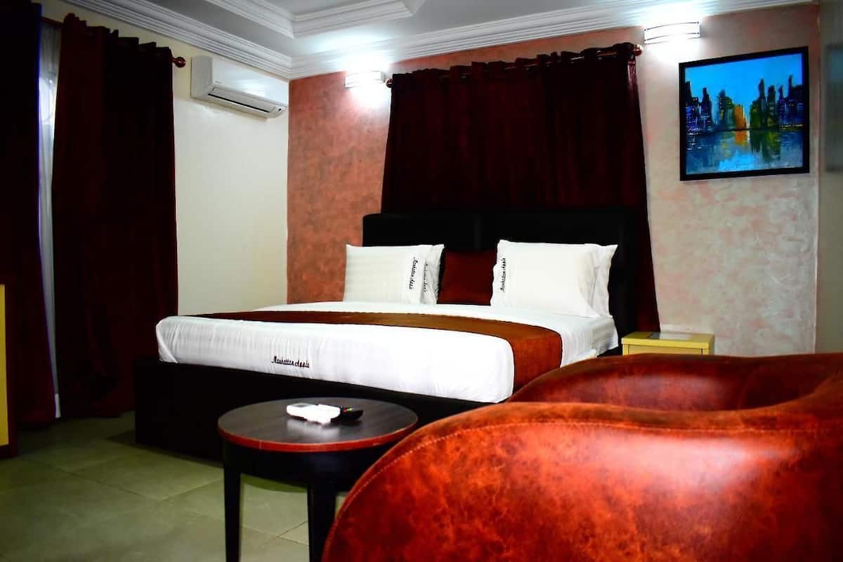 A hotel room with a bed, a red sofa, a small table, and a painting on the wall.