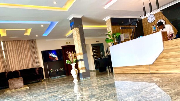 En hotellobby med receptionsdisk, en stor vase med planter, en tv-skærm og en sofa.