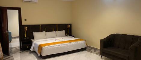 A hotel room with a large bed, a dark brown sofa, and a ceiling-mounted air conditioning unit.