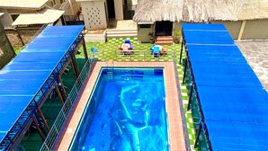 En rektangulær swimmingpool med en klar, blå vandoverflade, omgivet af en fliseterrasse og et skakmønster af grønne og hvide fliser.