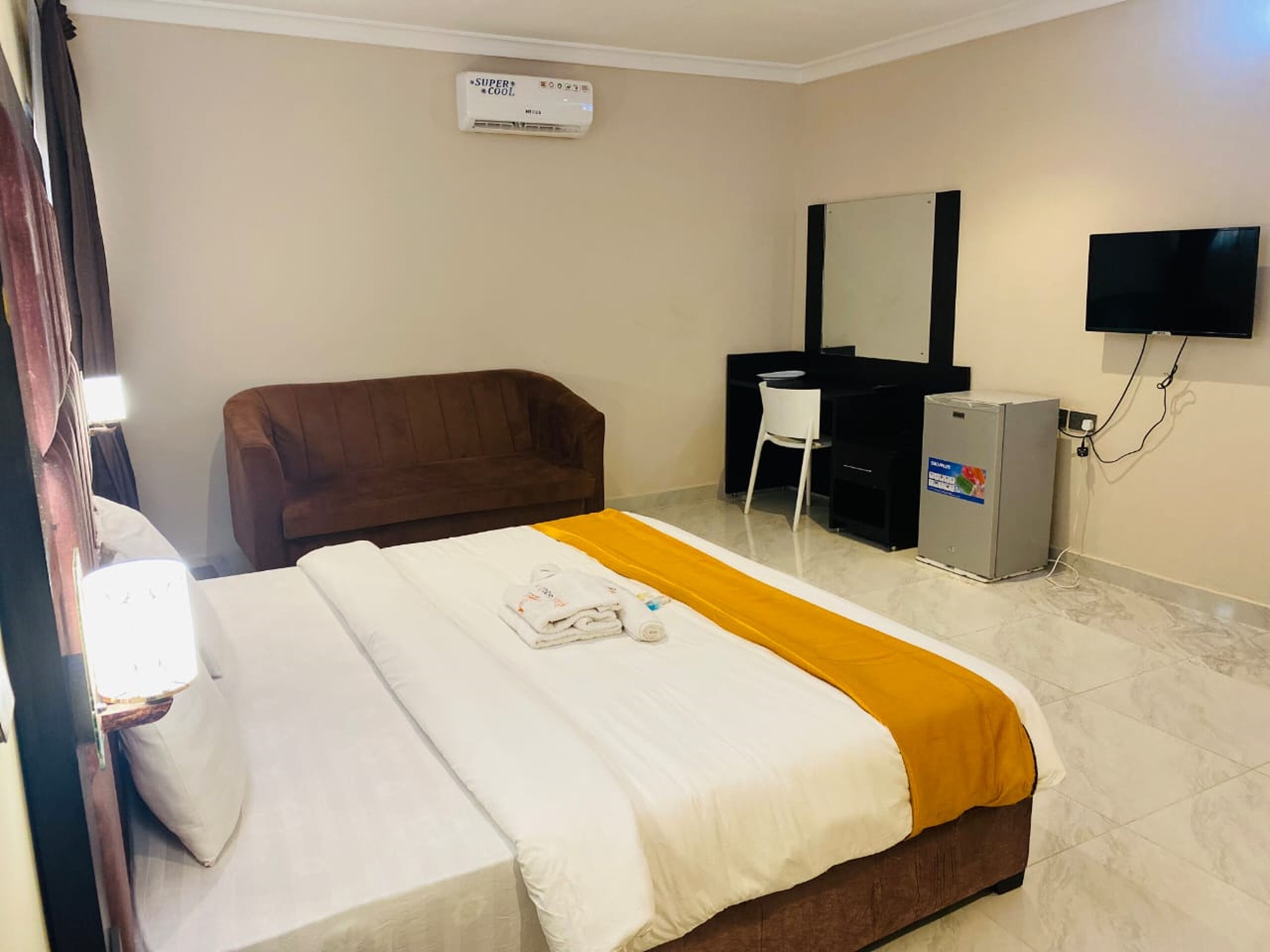 A hotel room with a bed, a brown sofa, a desk, a television, and a minibar.