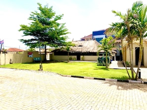 A courtyard with a thatched-roof building, a lawn, and a paved walkway. - Lylius Hotel (Ilorin)