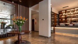 A modern hotel lobby with a reception desk, a round wooden table with a vase of flowers, and a decorative wall with patterned designs.