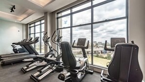 A gym with treadmills, elliptical machines, and a view of the city through large windows.