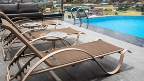 A poolside area with lounge chairs and a glass table, overlooking a swimming pool and a residential neighborhood. - Okash City Boutique Hotel (Nairobi)