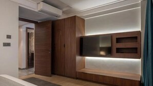 A modern bedroom with a built-in TV, wooden wardrobe, and a bench.