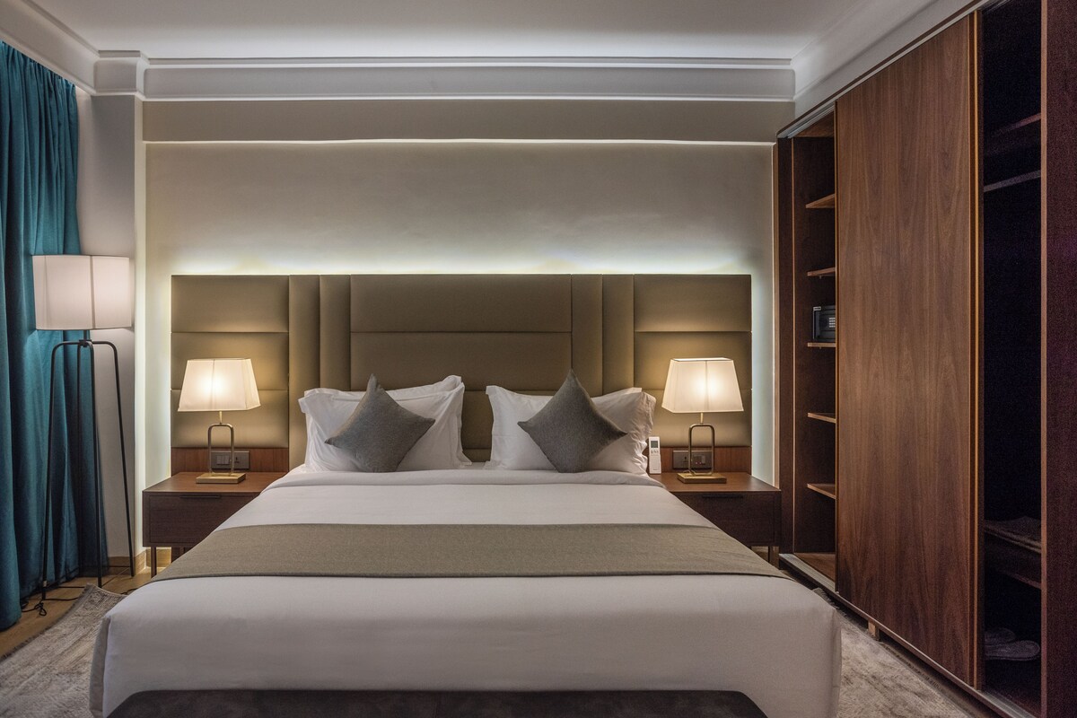 A large bed with a headboard, two bedside lamps, and a wardrobe.