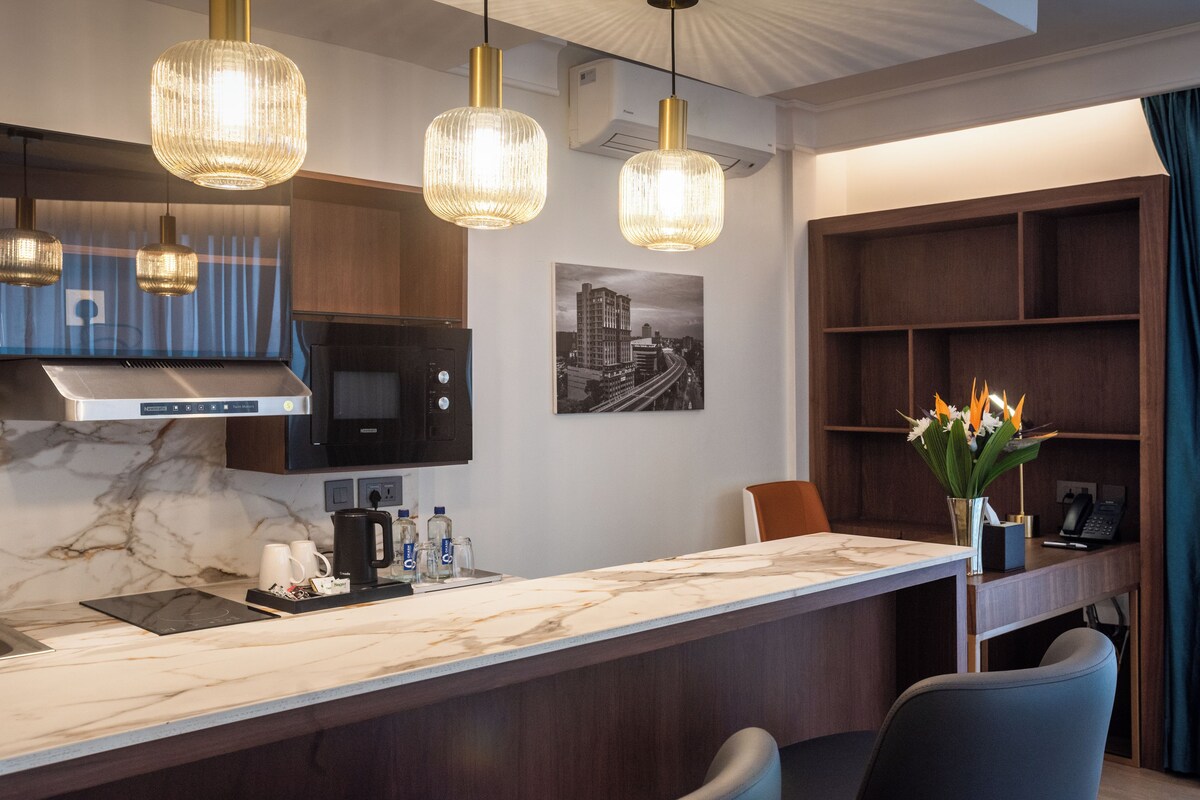 A modern kitchen with a marble countertop, stainless steel appliances, and pendant lighting.