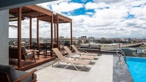 A rooftop terrace with lounge chairs, a pool, and a city view.