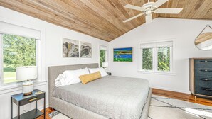 Une chambre à coucher comprenant un lit, une table de chevet, une lampe, un ventilateur de plafond et des œuvres d’art accrochées aux murs.