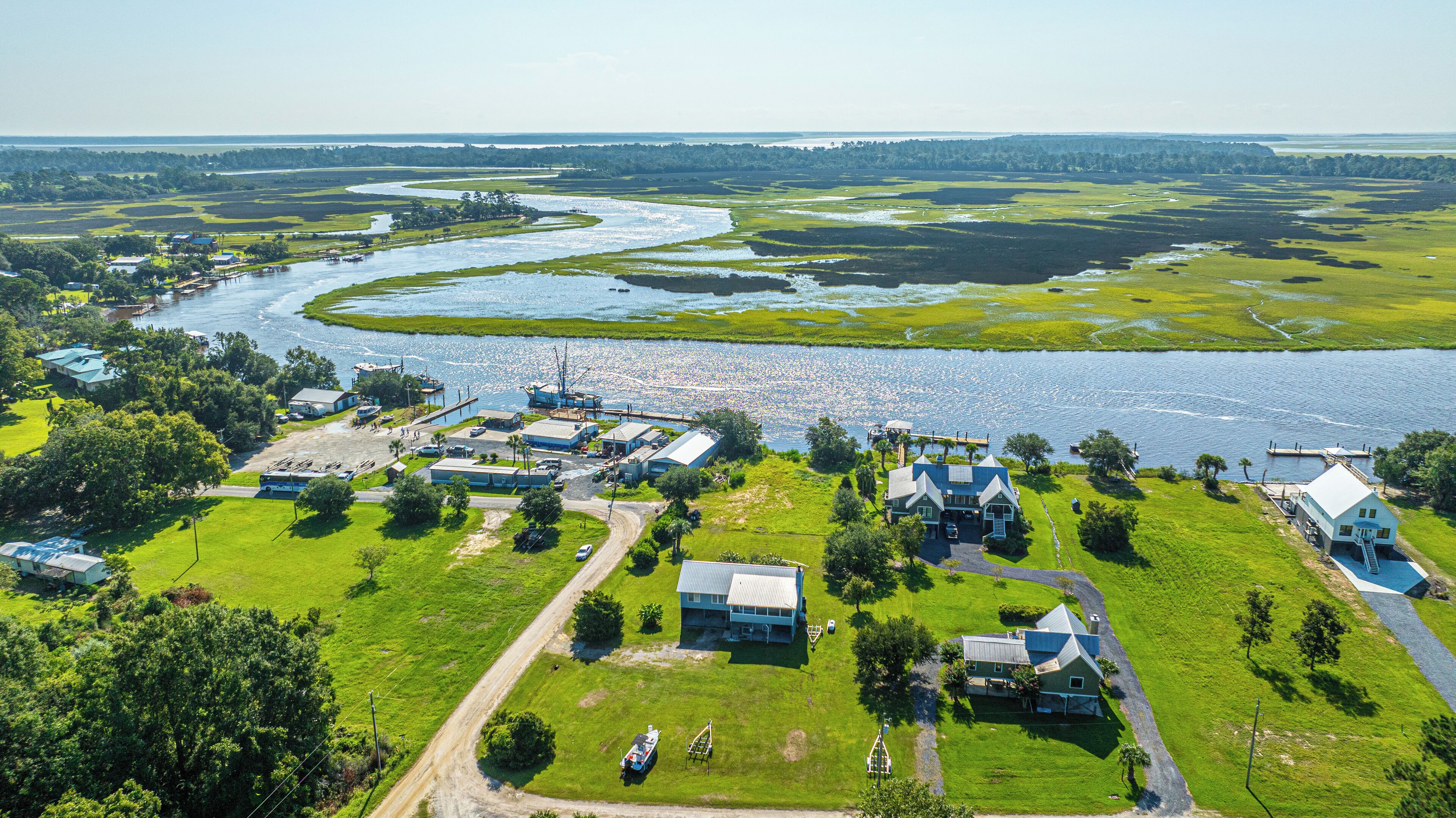 An aerial view of a riverside property with multiple buildings, a dock, and a boat.
