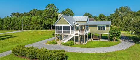 A two-story house with a porch and a deck, surrounded by a well-maintained lawn and trees.