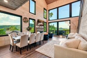 Uma sala de estar ampla com uma mesa de jantar, assentos confortáveis e janelas grandes com vista panorâmica.