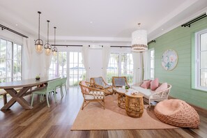 A spacious room with a large wooden dining table, wicker chairs, a round coffee table, and a sofa with cushions.