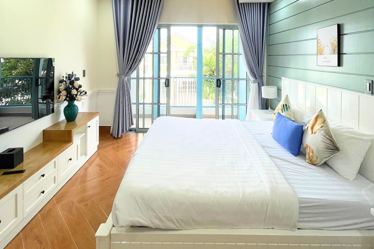 A bedroom with a bed, a TV, a console table, and a view of the outdoors.