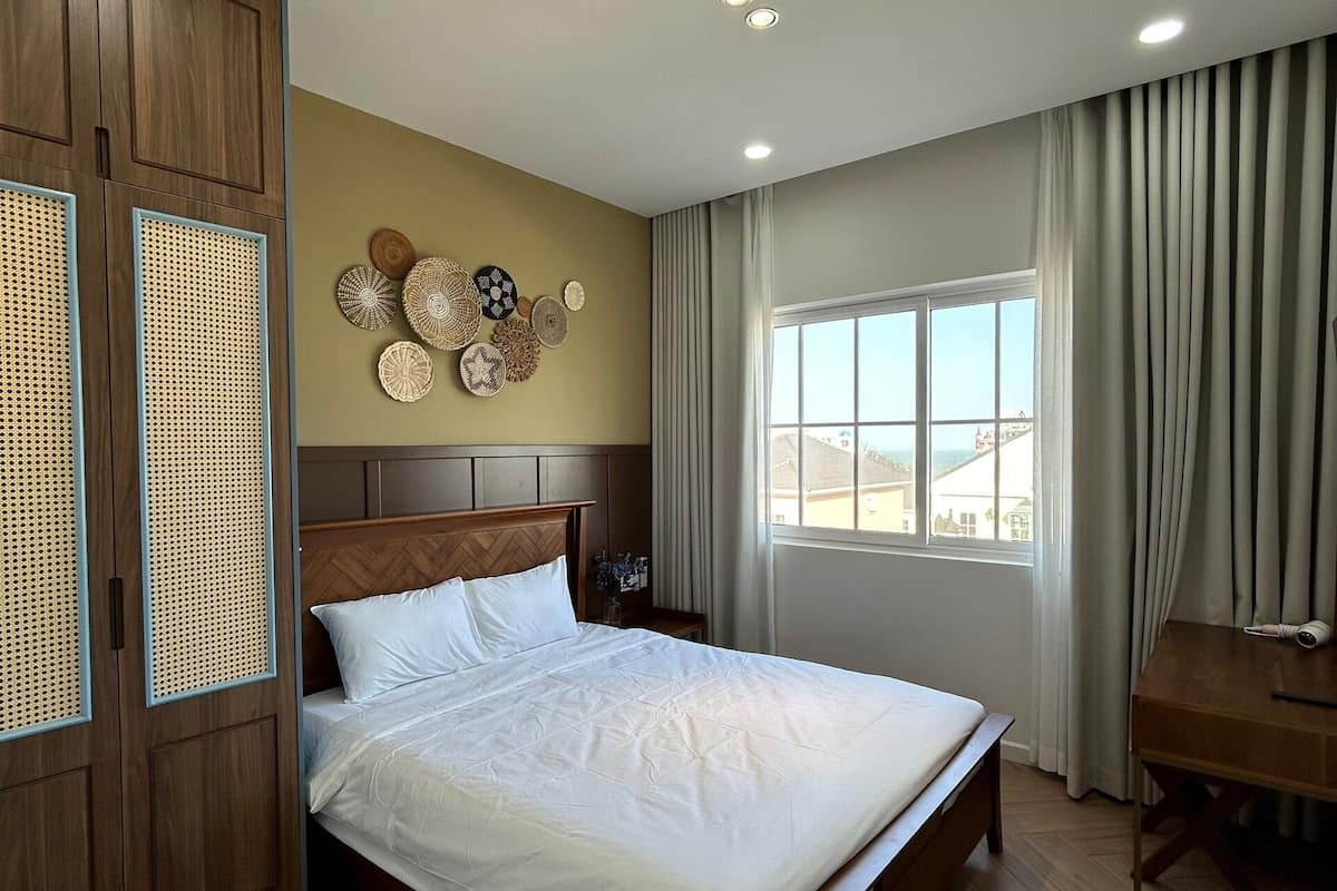 A spacious bedroom with a large bed, wooden wardrobe, and a view of the city through the window.