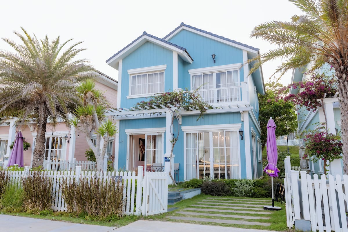 A two-story house with a white picket fence, a front porch, and a small garden area.