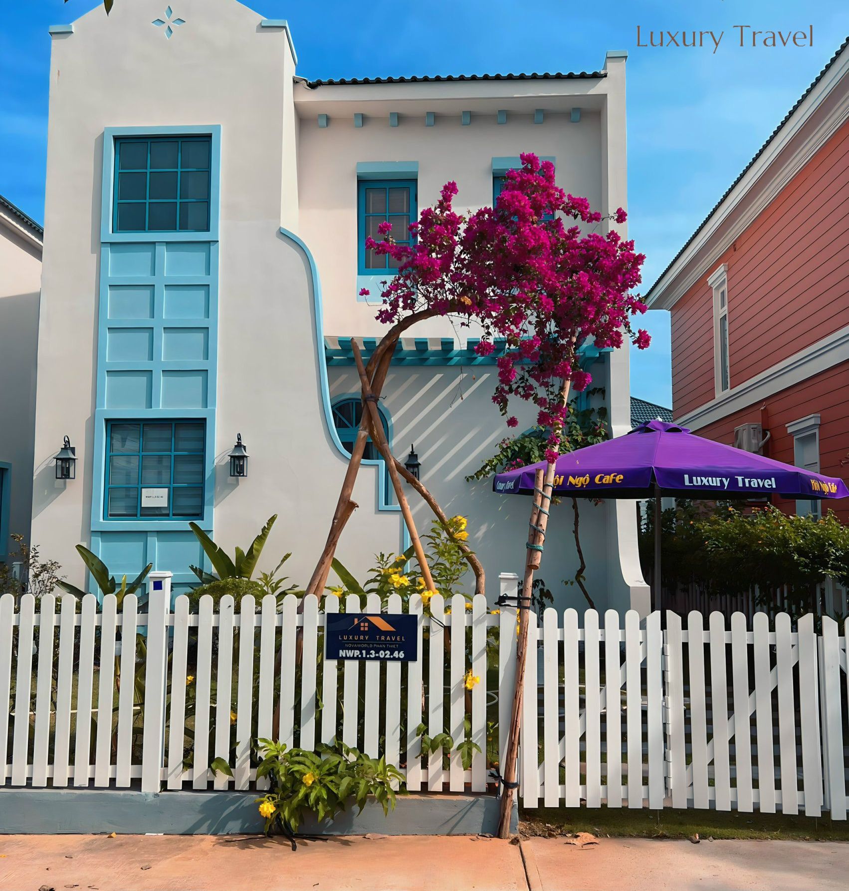 A white building with blue accents, a white picket fence, and a sign for 'Luxury Travel'.