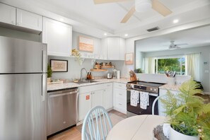 A modern kitchen with stainless steel appliances, white cabinetry, and a dining area with a table and chairs. - Dunedin Blue Bird Bungalow (Dunedin)