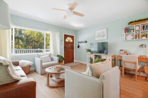 A living room with a sofa, armchairs, a coffee table, a TV, and a bookshelf. - Dunedin Blue Bird Bungalow (Dunedin)