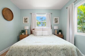 A bedroom with a bed, two bedside tables, a window with curtains, and framed artwork on the walls. - Dunedin Blue Bird Bungalow (Dunedin)