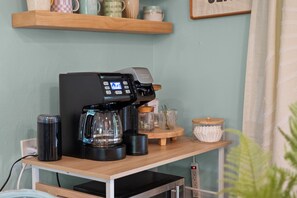 A coffee machine on a wooden table with a kettle, a cup, and a small shelf with mugs. - Dunedin Blue Bird Bungalow (Dunedin)