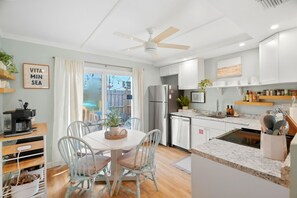 A modern kitchen with white cabinets, a built-in oven, and a dining area with a round table and chairs. - Dunedin Blue Bird Bungalow (Dunedin)
