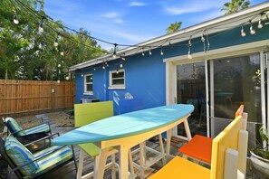 Ein Garten mit einem blauen Haus, einem Tisch, Stühlen und einer Holzterrasse.