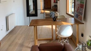 A modern living room with a wooden dining table, a brown leather sofa, and a glass coffee table.