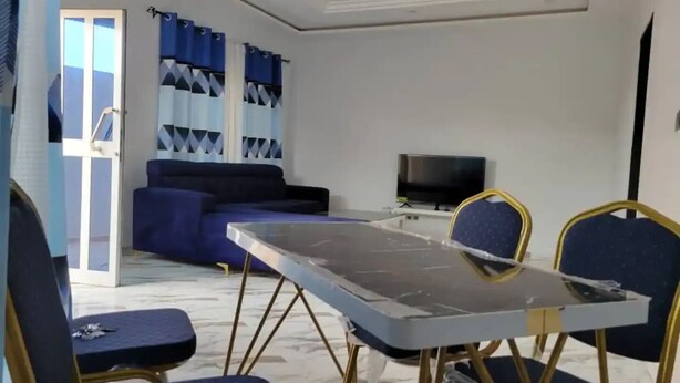 Uma sala de estar com sofá, televisão e mesa de jantar com cadeiras.