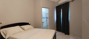 Quarto com cama, janela com cortinas e porta de acesso a um banheiro.