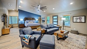A spacious living room with a large bed, leather sofas, a coffee table, and a ceiling fan.