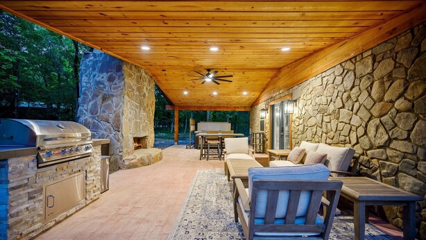 An outdoor patio with a stone wall, wooden ceiling, and a grill area.
