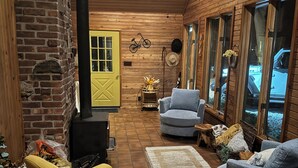 Interior acogedor de una cabaña con pared de ladrillo, techo de madera y una puerta amarilla. Se observan dos sillones, una mesita y una chimenea.