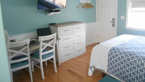 Een slaapkamer met een bed, een bureau met stoel, een dressoir, een aan de muur bevestigde televisie, en een deur.